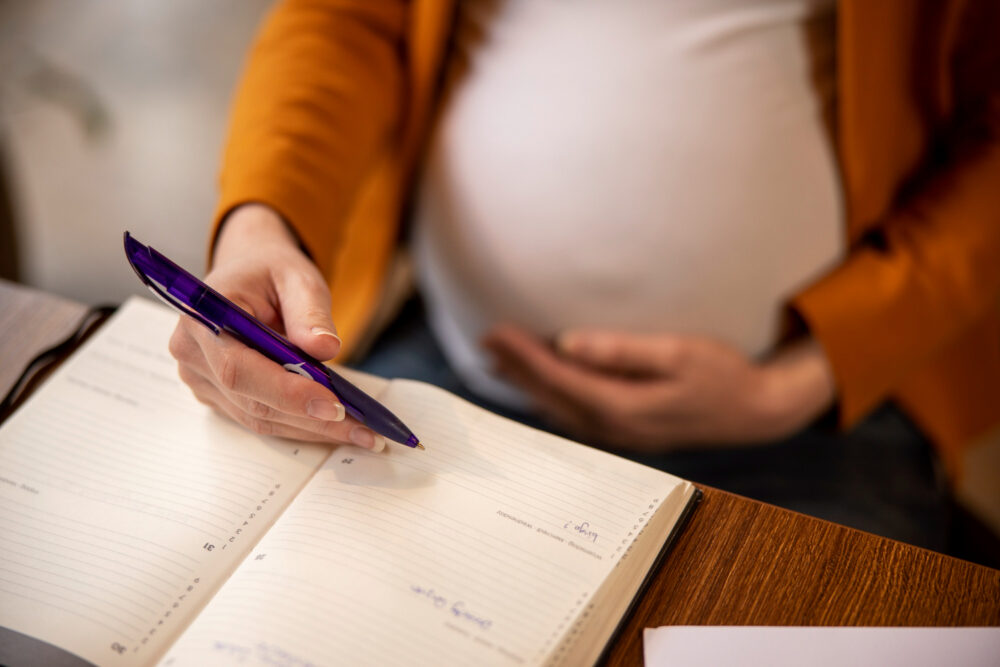a pregnant woman holding a phone with a book underneath