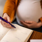 a pregnant woman holding a phone with a book underneath