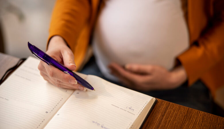 a pregnant woman holding a phone with a book underneath